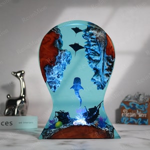 May include: A blue resin sculpture of a whale shark swimming in a coral reef. The sculpture is lit from below, creating a glowing effect. The base of the sculpture is made of wood.