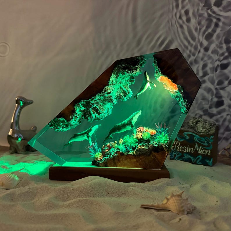 May include: A green resin sculpture of two whales swimming in a coral reef. The sculpture is lit from within, creating a glowing effect. The sculpture is mounted on a wooden base.