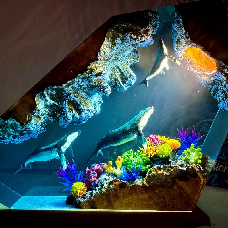 May include: A resin sculpture of a whale and coral reef, with a blue, green, and brown color scheme. The sculpture is lit from above, creating a glowing effect.