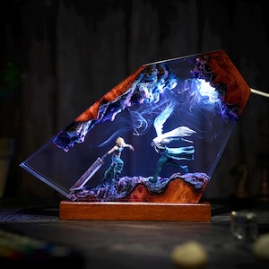 Peut inclure: Lampe décorative en résine représentant une scène de bataille avec deux personnages, sur fond de lumière bleue et violette. La lampe a une base en bois et une forme géométrique avec un cadre en bois.