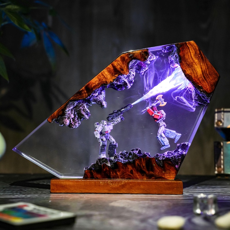 May include: A unique resin lamp featuring a battle scene with two robot figures. The lamp has a wooden base and a clear resin body with a wood grain top. The scene is illuminated with purple and white light, creating a dramatic effect.