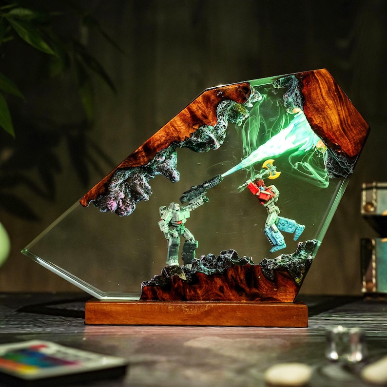 May include: A unique, illuminated resin art piece featuring a battle scene with two action figures. The artwork is encased in a clear, angled resin block with a wooden base and accents. The figures are in the middle of a battle, with a green light emanating from the top.