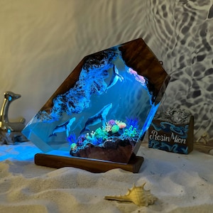 May include: A resin sculpture of a whale and coral reef, illuminated from below with blue light. The sculpture is encased in a clear resin block, mounted on a wooden base. The base is labeled "Resin Moon".