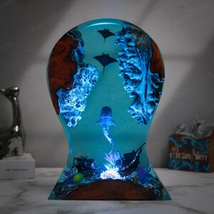 May include: A resin sculpture of a whale shark swimming in a blue ocean with coral reefs and two manta rays. The sculpture is illuminated from the bottom with a warm white light.