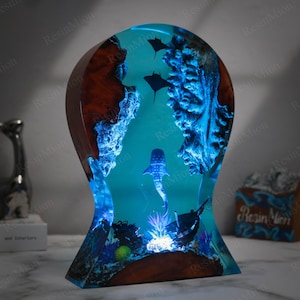 May include: A blue resin sculpture of a whale shark swimming through a coral reef. The sculpture is lit from the bottom, creating a glowing effect. The sculpture is made of wood and resin and is approximately 30 cm tall.