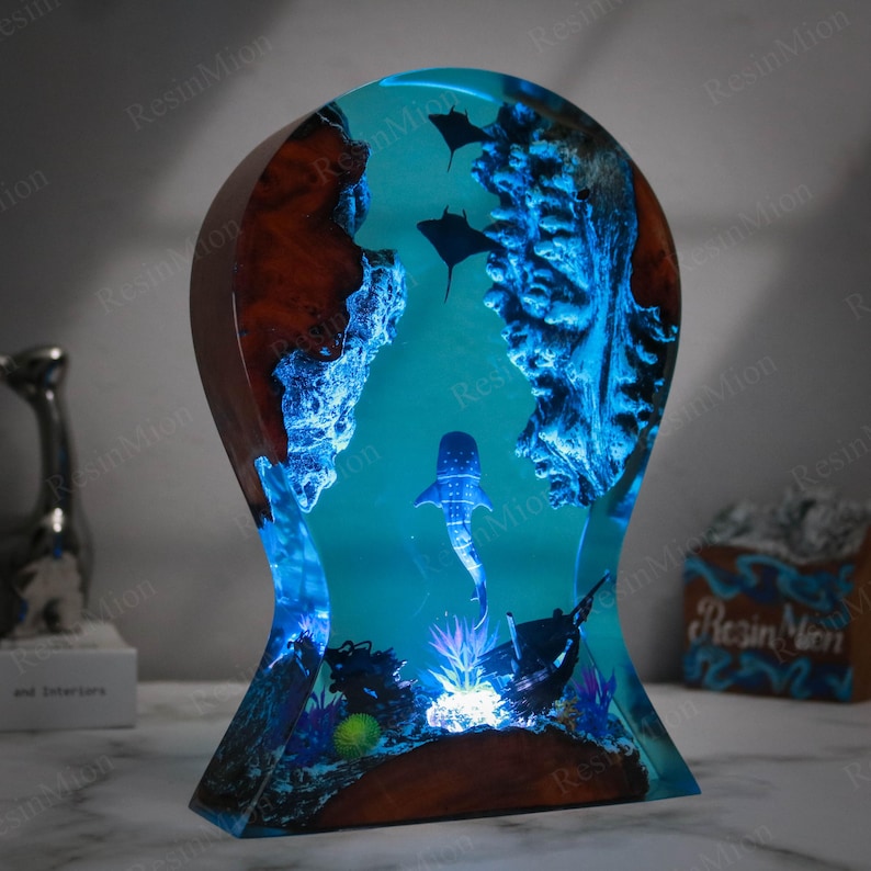 May include: A blue resin sculpture of a whale shark swimming through a coral reef. The sculpture is lit from the bottom, creating a glowing effect. The sculpture is made of wood and resin and is approximately 30 cm tall.