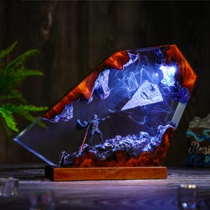 May include: A Star Wars resin lamp featuring Darth Vader with a red lightsaber, a Star Destroyer, and a smoky blue and orange design. The lamp is set on a wooden base.