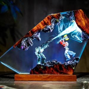 May include: A unique resin art piece featuring a battle scene between two robot figures. The artwork is encased in a clear, angled resin block with a wooden base. The figures are set against a blue and purple background with a beam of light.