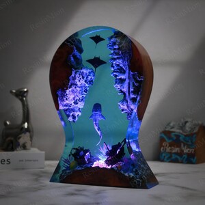 May include: A resin sculpture of a whale shark swimming through a coral reef with manta rays above. The sculpture is illuminated with blue LED lights and is set on a wooden base.