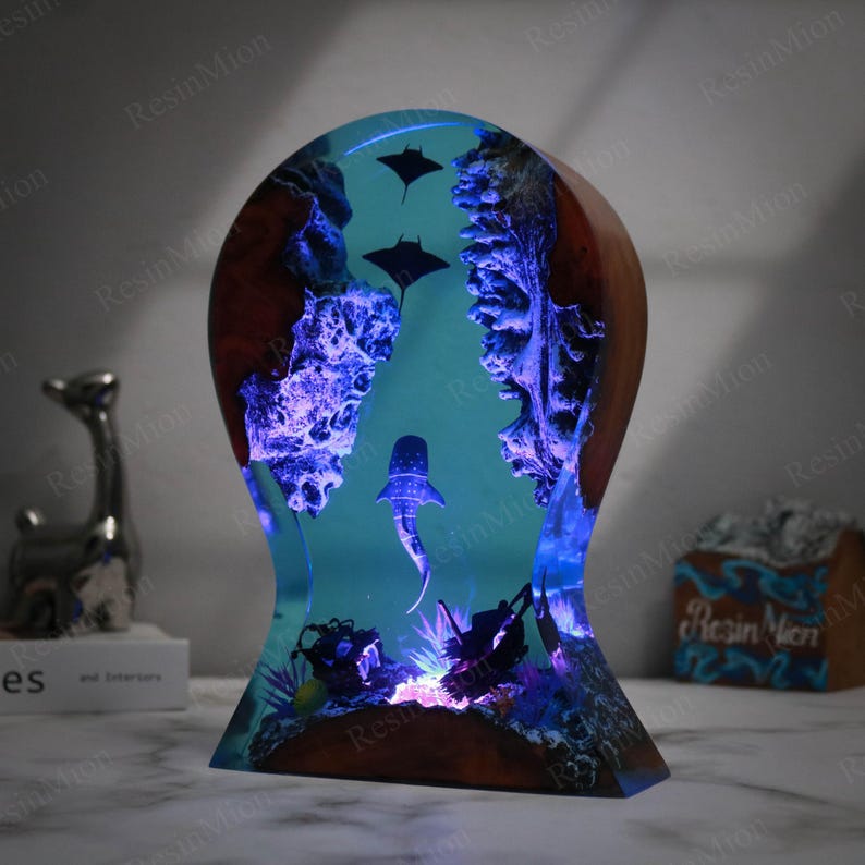 May include: A resin sculpture of a whale shark swimming through a coral reef with manta rays above. The sculpture is illuminated with blue LED lights and is set on a wooden base.