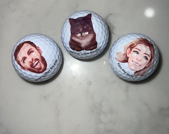 May include: Three white golf balls with different designs. One ball has a cartoon image of a person with the text "Best golfer by far". Another ball has a cartoon image of a cat with the text "Where's the birdie?". The third ball has a cartoon image of a person with the text "Kiss my putt".