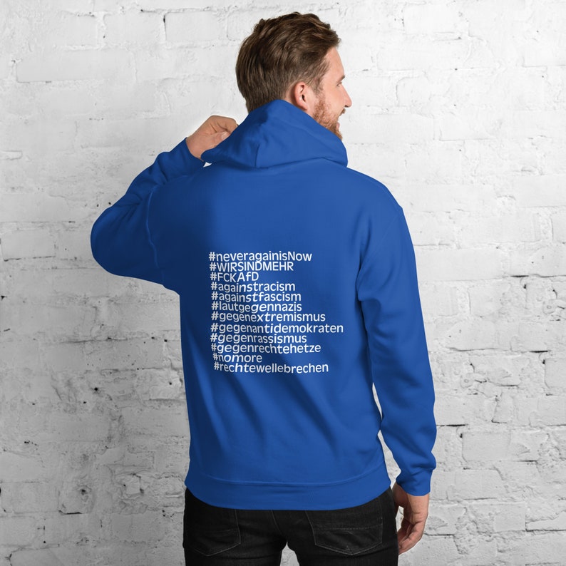 May include: A royal blue hoodie with a white print on the back. The print includes the hashtags #neveragainisnow, #wirsindmehr, #fckafd, #againstracism, #againstfascism, #lautgegennazis, #gegenextremismus, #gegenantidemokraten, #gegenrassismus, #gegenrechtehetze, #nomore, #rechtewellebrechen.