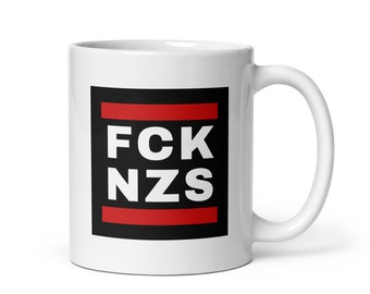 May include: White ceramic mug with a black square containing the text "FCK NZS" in white letters with a red horizontal line above and below the text.
