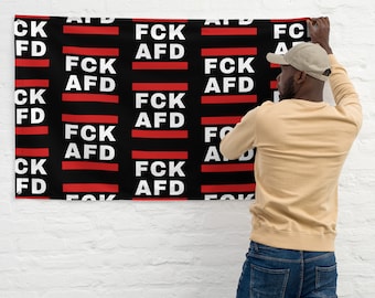 May include: A black and red flag with the text "FCK AFD" repeated across the surface. A person is hanging the flag on a white brick wall.
