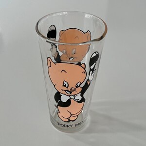 May include: A clear glass with a cartoon image of Porky Pig wearing a tuxedo and holding a top hat. The glass has the text "Porky Pig" printed on the bottom.