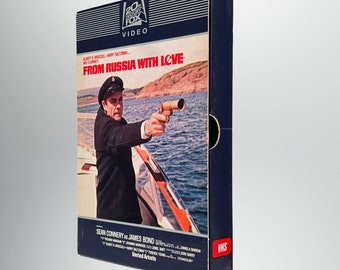 Könnte beinhalten: Ein VHS-Kassetten-Etui für den Film "Liebesgrüße aus Moskau" mit Sean Connery als James Bond. Das Cover zeigt eine Szene, in der James Bond auf einem Boot eine Waffe hält.