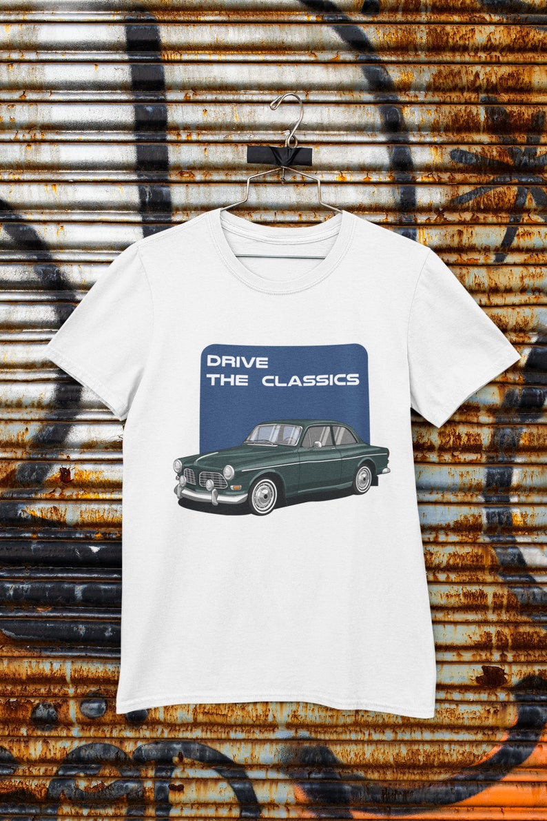 May include: White t-shirt featuring a blue rectangle with the text "DRIVE THE CLASSICS" and an illustration of a green vintage Volvo car.