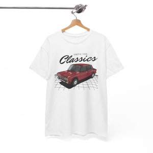 Puede incluir: Camiseta blanca con una ilustración de un coche vintage rojo y el texto "Drive the Classics" impreso en la parte delantera.