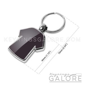 May include: A black and silver T-shirt shaped keychain. The keychain is 1.5 inches wide and 2.75 inches long. The text "KEYRINGSGALORE.COM" is visible. The keychain has a silver key ring.