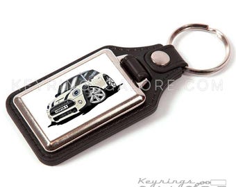 May include: A white Mini Cooper S car keychain with a black leather strap and a silver metal key ring. The keychain features a cartoon-style illustration of the car.