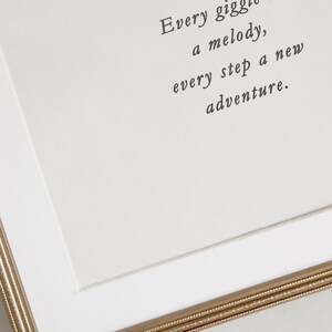 Op de afbeelding: Een witte ingelijste print met de tekst "Every giggle a melody, every step a new adventure."