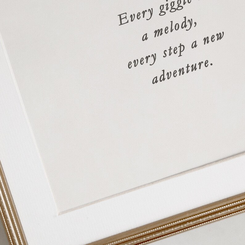 Op de afbeelding: Een witte ingelijste print met de tekst "Every giggle a melody, every step a new adventure."