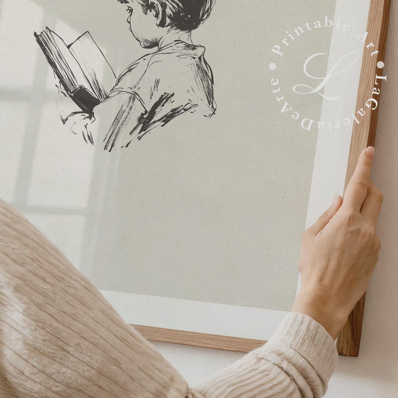 May include: A black and white illustration of a child reading a book. The illustration is framed in a light wood frame. The frame is being held by a hand.