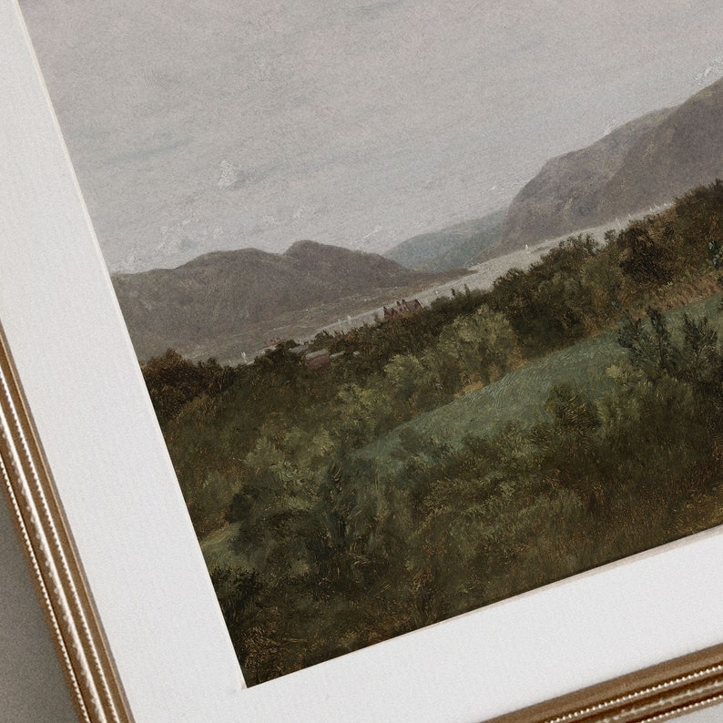 May include: A framed painting depicting a landscape with a river winding through a valley. The mountains in the distance are covered in a soft, hazy light, while the foreground is filled with lush green trees and foliage.