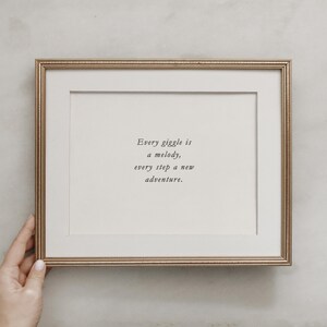 Op de afbeelding: Een gouden ingelijste print met de quote "Elke giechel is een melodie, elke stap een nieuw avontuur."