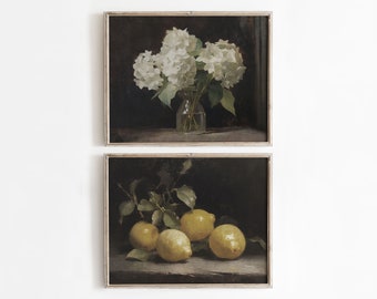 May include: Two framed still life paintings. The top painting features a bouquet of white hydrangeas in a clear glass vase on a dark brown surface. The bottom painting features a cluster of yellow lemons with green leaves on a dark brown surface.
