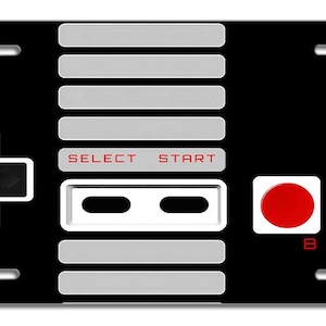 May include: Black and white license plate with a retro video game controller design. The controller has a white plus sign button, two gray buttons labeled "SELECT" and "START", two gray buttons with black circles, and two red buttons labeled "B" and "A".