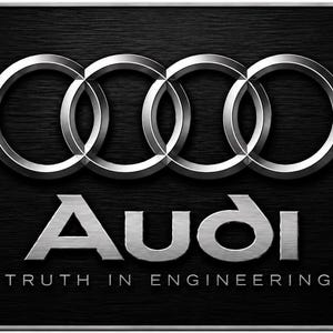 May include: A rectangular license plate featuring a black brushed metal background with a red honeycomb pattern on the sides. The silver Audi logo and the text Audi Truth in Engineering are centered on the plate, which has four mounting holes.