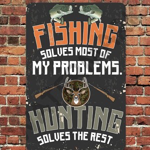 May include: A black and gray metal sign with a distressed look. The sign features a fishing scene with two fish and the text "Fishing solves most of my problems. Hunting solves the rest."