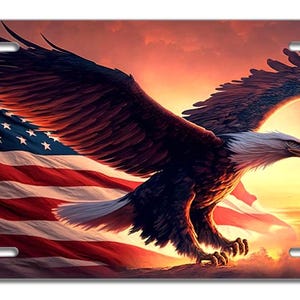 May include: A bald eagle with its wings spread wide soars above an American flag waving in the wind. The eagle is flying towards a bright orange and yellow sunset.