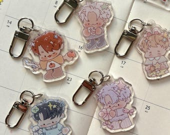 May include: A collection of six acrylic charm keychains featuring cute anime-style characters in various poses. Each keychain has a silver-colored clasp. The characters have different hair colors and outfits, with some holding objects like a teddy bear or a heart.