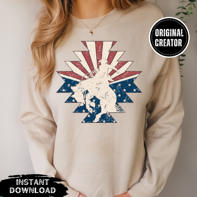 May include: A beige sweatshirt with a vintage-style graphic of a cowgirl riding a horse in front of a red, white, and blue American flag design.