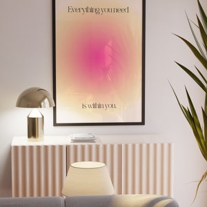 K&ouml;nnte beinhalten: Ein gerahmter Kunstdruck mit dem Text "Everything you need is within you" vor einem rosa-gelben Farbverlauf. Der Druck h&auml;ngt &uuml;ber einem hellrosa Schrank mit einer goldenen Lampe und einem wei&szlig;en Lampenschirm. Rechts ist eine gr&uuml;ne Pflanze zu sehen.