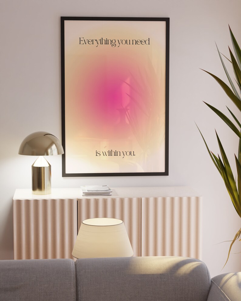 K&ouml;nnte beinhalten: Ein gerahmter Kunstdruck mit dem Text "Everything you need is within you" vor einem rosa-gelben Farbverlauf. Der Druck h&auml;ngt &uuml;ber einem hellrosa Schrank mit einer goldenen Lampe und einem wei&szlig;en Lampenschirm. Rechts ist eine gr&uuml;ne Pflanze zu sehen.