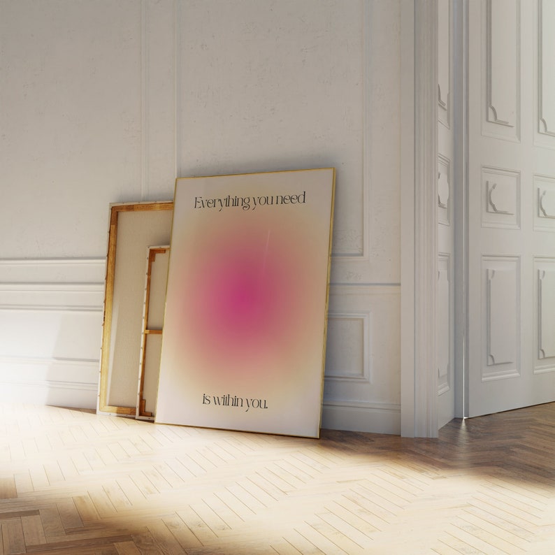 K&ouml;nnte beinhalten: Ein gerahmtes Poster mit dem Text "Everything you need is within you" vor einem Hintergrund aus Rosa- und Cremet&ouml;nen. Das Poster lehnt an einer wei&szlig;en Wand, neben anderen gerahmten Kunstwerken. Der Raum hat einen Holzboden.