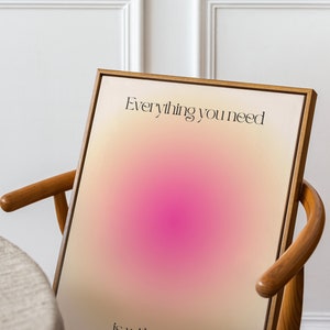 K&ouml;nnte beinhalten: Ein gerahmter Kunstdruck mit einem Farbverlauf aus Beige, Rosa und Wei&szlig;. Der schwarze Text lautet "Everything you need is within you". Das Kunstwerk wird auf einem Holzstuhl pr&auml;sentiert.