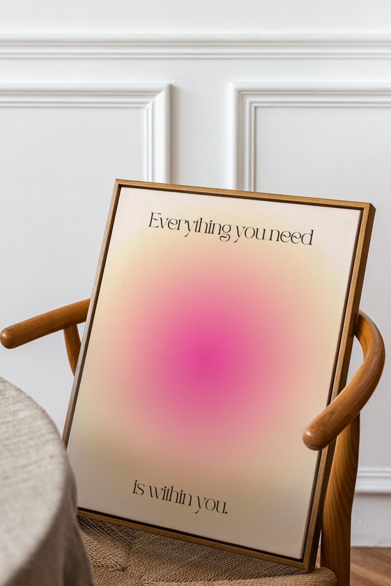 K&ouml;nnte beinhalten: Ein gerahmter Kunstdruck mit einem Farbverlauf aus Beige, Rosa und Wei&szlig;. Der schwarze Text lautet "Everything you need is within you". Das Kunstwerk wird auf einem Holzstuhl pr&auml;sentiert.