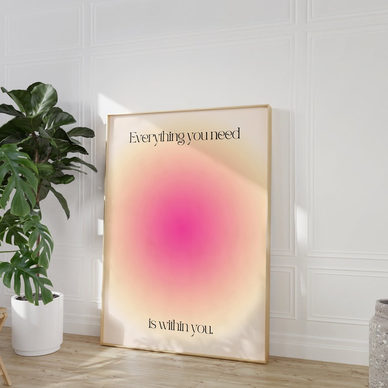K&ouml;nnte beinhalten: Gerahmtes Poster mit einem Farbverlauf in Rosa und Gelb. Der minimalistische Text lautet "Everything you need is within you". Das Poster lehnt an einer wei&szlig;en Wand, mit einer Topfpflanze im Hintergrund.