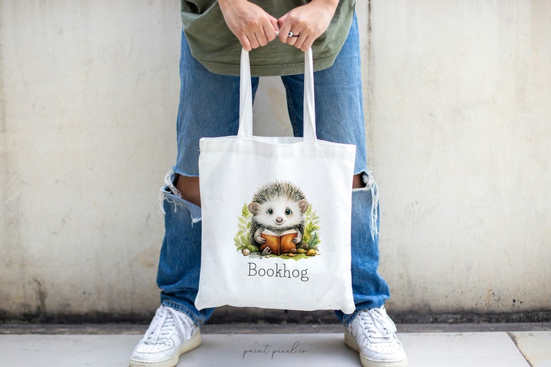 May include: White tote bag with a cartoon hedgehog reading a book. The bag has the text "Bookhog" printed on it.