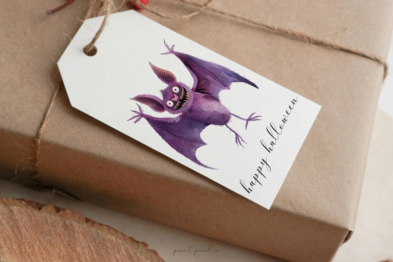Puede incluir: Una etiqueta de regalo blanca con un murci&eacute;lago de dibujos animados morado con ojos grandes y el texto "happy halloween" en escritura cursiva negra.