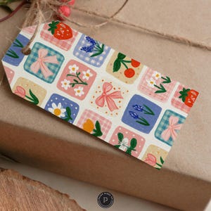 Puede incluir: Una etiqueta de regalo rectangular con un patr&oacute;n de cuadr&iacute;cula repetitivo de cuadrados coloridos. Cada cuadrado contiene ilustraciones de fresas, lazos rosas, margaritas, cerezas, flores azules y tulipanes sobre fondos a cuadros o pastel.