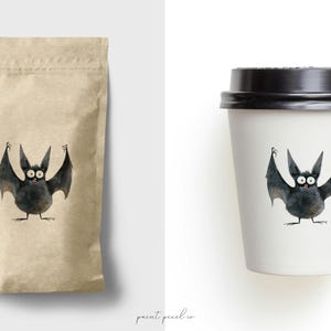 Puede incluir: Una bolsa de papel marr&oacute;n y una taza de caf&eacute; blanca con tapa negra, ambas con una ilustraci&oacute;n de dibujos animados de un murci&eacute;lago negro con ojos grandes y una amplia sonrisa.