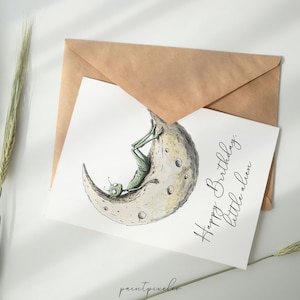 Puede incluir: Una tarjeta blanca con un extraterrestre verde sentado en una luna creciente. El texto en la tarjeta dice "Feliz cumplea&ntilde;os, peque&ntilde;o extraterrestre."