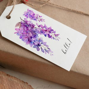 May include: A white gift tag with a watercolor illustration of purple wisteria flowers and the word "hello!" in black script.