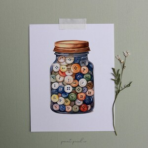 May include: A watercolor painting of a glass jar filled with colorful buttons. The jar has a brown lid and the buttons are various shades of blue, green, yellow, orange, and white.