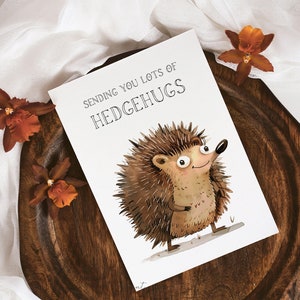 May include: A white card with the text "Sending you lots of Hedgehugs" and a cartoon illustration of a brown hedgehog with big eyes and a smile.